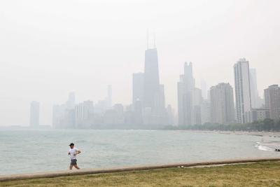 A jogger runs along the shoreline of Lake Michigan, with heavy smoke from the Canadian wildfires in the background, in June 2023.