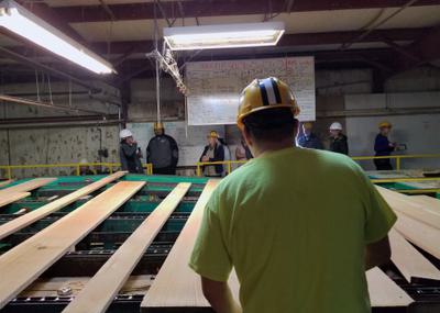 An inspector grades lumber at the Menominee sawmill, with visitors on tour in the background.